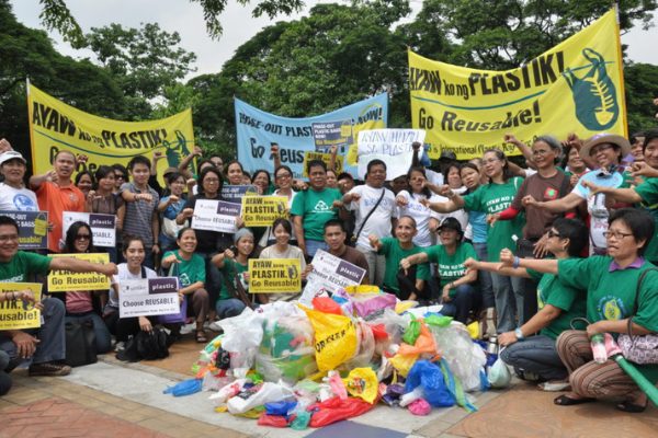 Group of Asian people protesting against plastic pollution. There's a pile of plastic bags in front of them, they are holding signs.