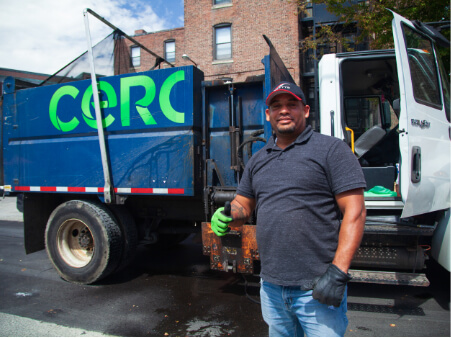 Trabajador posando frente a un camión de reciclaje con el pulgar hacia arriba.