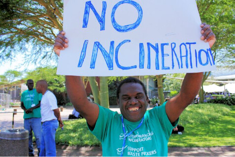 Man smiling while holding a no incineration poster above his head.