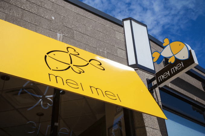 Close up of a resturant's sign. Yellow sign with a fish as a logo and the words mei mei