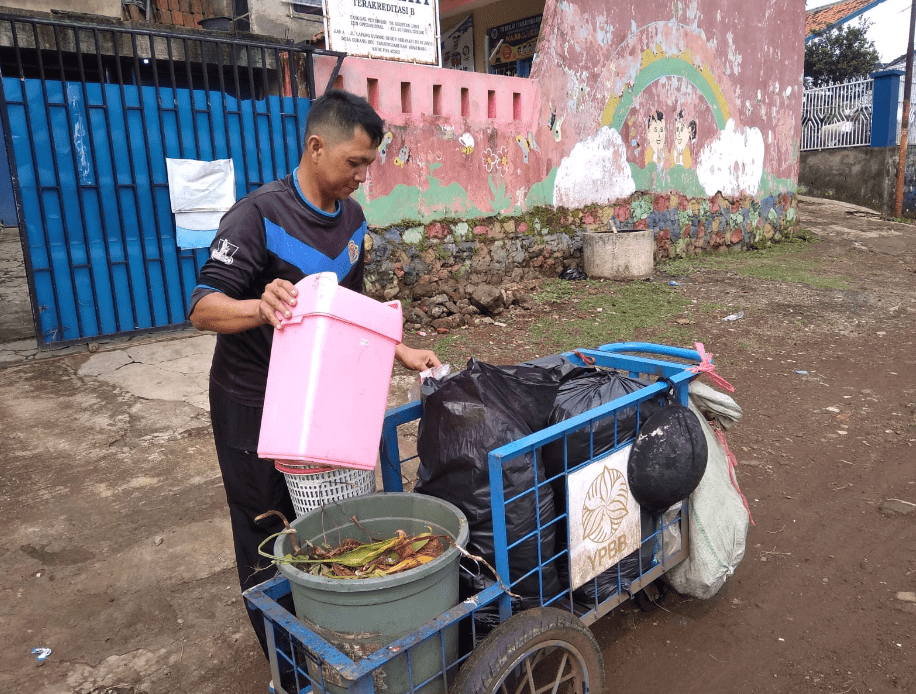 عامل نفايات في باندونغ، إندونيسيا يجمع النفايات المنفصلة من المصدر، وشوهد وهو ينقل النفايات العضوية من سلة مهملات أحد السكان إلى عربة التجميع الخاصة به.