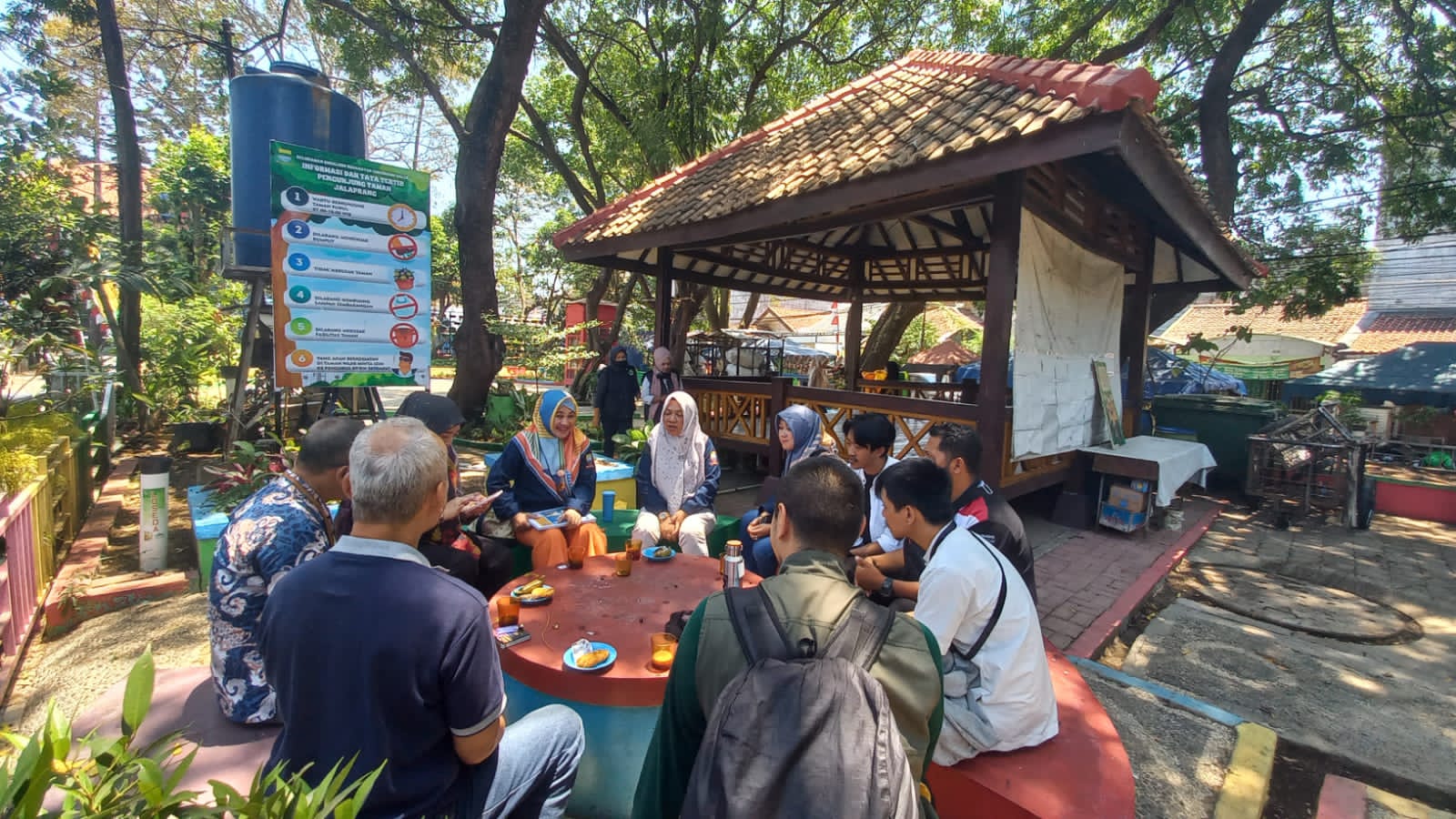 Nueve miembros de AZWI y DLH se sientan alrededor de una mesa de hormigón en un espacio público abierto en Bandung.
