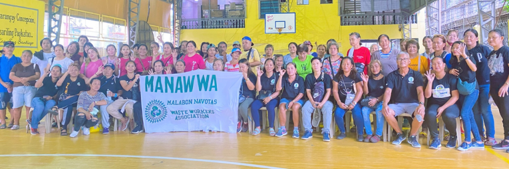 A group of people is sitting in a basketball court, holding up a banner.