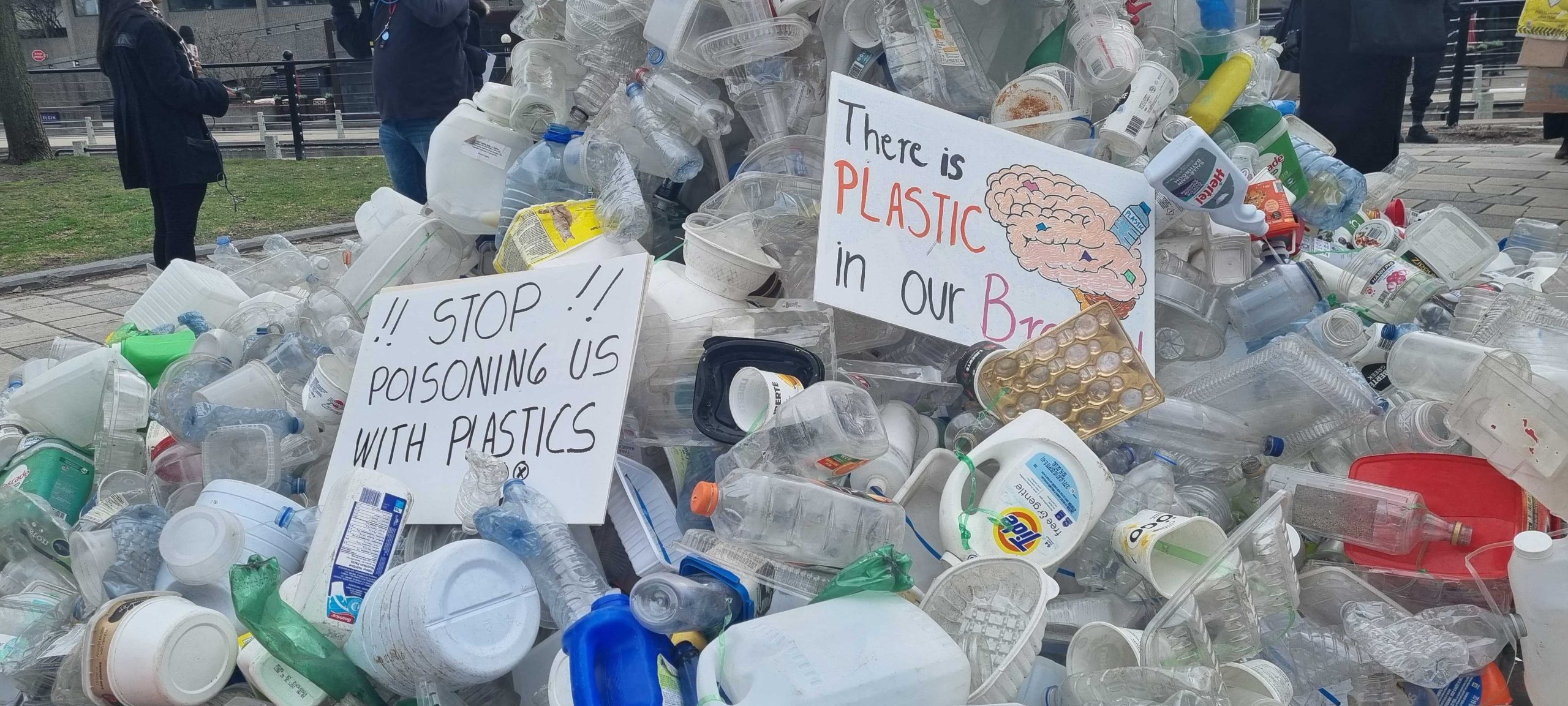 a hill of plastic bottles and other plastic waste with a placard that says: Stop poisoning us with plastics