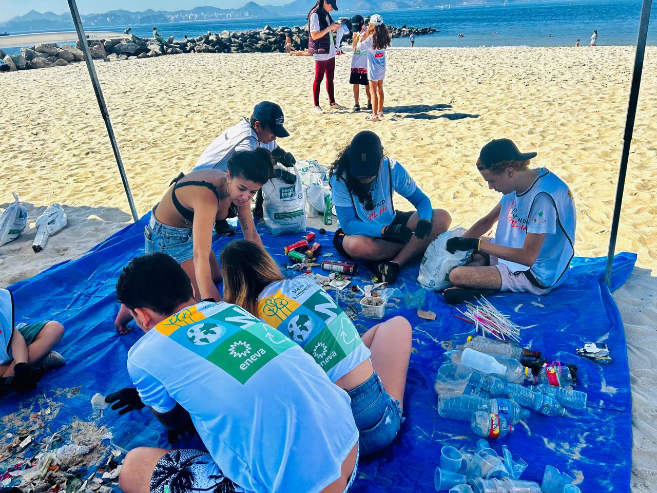 Grupo de personas clasificando plásticos en una superficie azul en una playa.